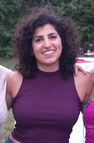 Samah is smiling; she is wearing a sleeveless purple shirt and has her arms around two friends that are not in the frame.